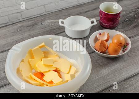 Preparazione di torte - coppa in plastica con la farina e il tuorlo, gusci delle uova e sale in sfondo grigio sulla tavola di legno. Foto Stock