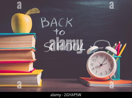 accessori per la scuola sul tavolo con sfondo lavagna. Matite e libri Foto Stock