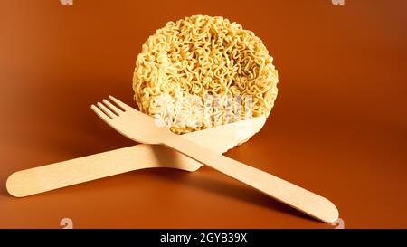 Tagliatelle istantanee crude a forma di cerchio con forchetta a perdere in legno. Pasta, per la preparazione della quale è sufficiente versare acqua bollente e. Foto Stock