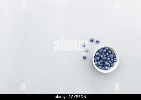 Piatto posare su fondo grigio in cemento con ciotola di mirtillo fresco. Area di spazio di copia per il testo. Sano concetto di cibo vegetariano. Vitamine da naturale Foto Stock