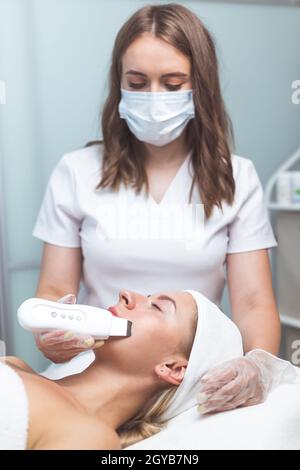 Il cosmetologo professionista usa la fonoforesi per pulire il volto di una cliente femminile. Bellezza e salute della pelle Foto Stock