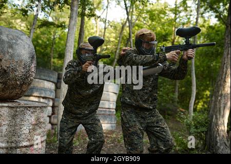 Paintball giocatori in uniforme e maschere giocare sul parco giochi nella foresta. Sport estremo con arma pneumatica e pallottole o pennarelli, militare Foto Stock