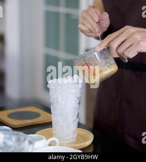 Tazza in plastica trasparente con ghiaccio per il caffè ghiacciato sul tavolo. Barista professionista che prepara il caffè al banco. Foto Stock