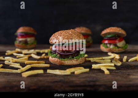 Hamburger con pomodori, cipolle, cetrioli, lattuga, formaggio fuso e patatine fritte serviti su un rustico tavolo di legno Foto Stock