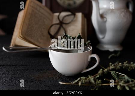 Festa del tè. Tazza di tè e teiera su tavolo di legno con vecchio orologio e libro in background Foto Stock