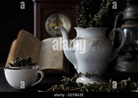 Festa del tè. Tazza di tè e teiera su tavolo di legno con vecchio orologio e libro in background Foto Stock