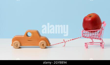 una macchina per bambini in legno tira un carrello in ferro con una mela su una corda. Cibo sano, consegna di cibo Foto Stock