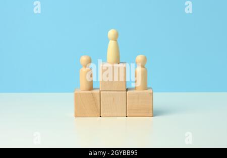 figure di uomini in legno si trovano su un piedistallo dei loro cubetti su uno sfondo blu. Il concetto di rivalità nello sport, nel business e nella vita. Raggiungere il successo Foto Stock