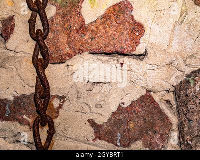 Vecchia catena di ferro arrugginita sullo sfondo di un muro di granito. Maglie di una catena metallica. Muro di concessione. Pietre di granito. Muratura di cemento. Immagine di sfondo. Luogo Foto Stock