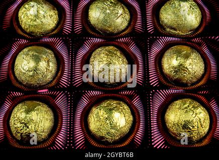 Una scatola di cioccolatini in un involucro di lamina dorata. Dolci in lamina lucida. Colore dorato. Dolce dessert. Scatola di dolci. Cibo dolce. Sfondo nero. Pacchetto Foto Stock