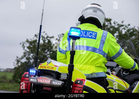 Vista posteriore dell'ufficiale di polizia fermo mentre sulla Police Motorbike con le luci di emergenza blu accese Foto Stock