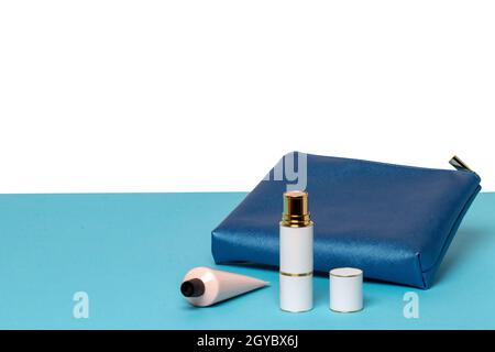 Composizione decorativa di una borsa da viaggio cosmetica blu femminile e bottiglie di prodotti cosmetici su scrivania blu isolate su sfondo bianco. Modello per Foto Stock