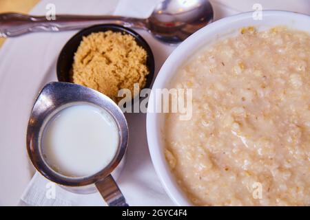 Guardando giù su tradizionale e pulito ciotola di farina d'avena calda della colazione con lato dello zucchero di canna e del latte Foto Stock