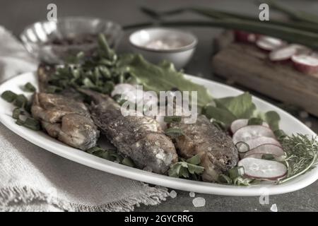 Su un piatto di crogiolo fritto, ravanelli, cipolle verdi e foglie di lattuga. Vista frontale, primo piano. Il concetto di nutrizione naturale. Foto Stock