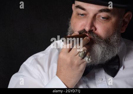 Ritratto di un uomo con un sigaro e una barba in una stanza buia Foto Stock