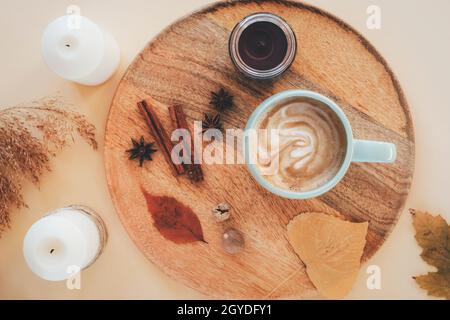 Una tazza di cappuccino con anice stellato, noce moscata e bastoncini di cannella su un vassoio di legno piatto d'autunno, bevanda calda, casa accogliente. Vista dall'alto. Foto Stock