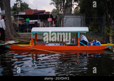 Tradizionale trajinera arancione nel lago di Xochimilco con alberi come sfondo Foto Stock