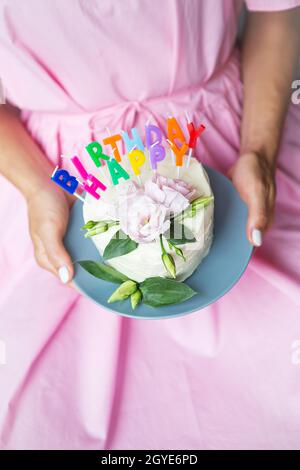 torta di compleanno felice con lettere compleanno felice sotto forma di candele, una ragazza molto colorata e molto gustosa in un vestito rosa tiene nelle sue mani. Holida Foto Stock