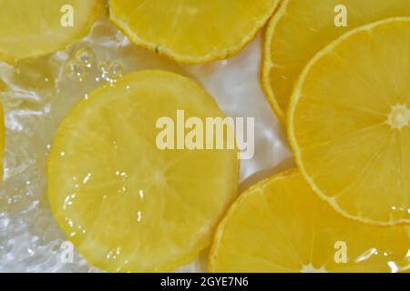 Vista ravvicinata delle fette di limone gialle sullo sfondo della limonata. Texture di rinfrescante dolce d'estate con macroflicine sulla parete di vetro. De. Piatta Foto Stock