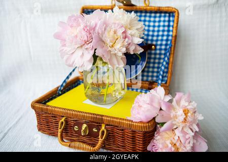 Un bellissimo mazzo di peonie rosa sorge in un vaso su una valigia di legno. Bella composizione. Foto Stock