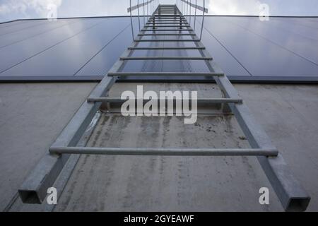 Fuga dal fuoco sull'edificio industriale sopra, vista dal basso. Corrimano in acciaio inox, scala per tetti. Vista in dettaglio delle scale con gabbia di sicurezza. Edificio con co Foto Stock