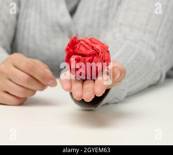 la mano femmina contiene una sfera di carta rossa sbriciolita. Nuova idea, brainstorming Foto Stock
