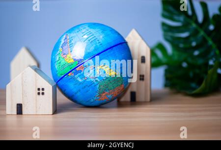 Una casa modello in legno è posta accanto ad un globo replica. Posto su un tavolo in legno con uno sfondo grigio chiaro. Salvare il concetto di mondo Foto Stock