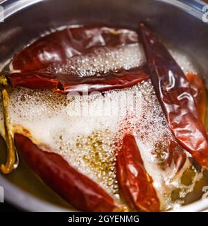 Peperoni rossi secchi bollenti in olio all'interno della pentola di cottura Foto Stock