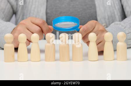 figurine di uomini su un tavolo bianco, una mano femminile tiene una lente d'ingrandimento su uno. concetto di ricerca di dipendenti in azienda, reclutamento di pers Foto Stock