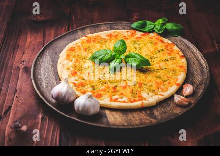 Pane per pizza con aglio, formaggio e basilico su sfondo ligneo Foto Stock