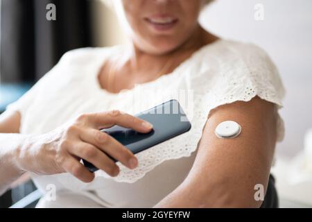 Donna che verifica il livello di glucosio con il monitoraggio continuo del glucosio su dispositivi mobili Telefono Foto Stock