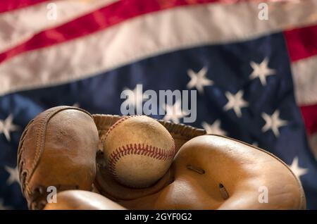 Il primo piano di un vecchio baseball e di un guanto contro la bandiera americana mette in evidenza uno degli sport più popolari del paese. Foto Stock