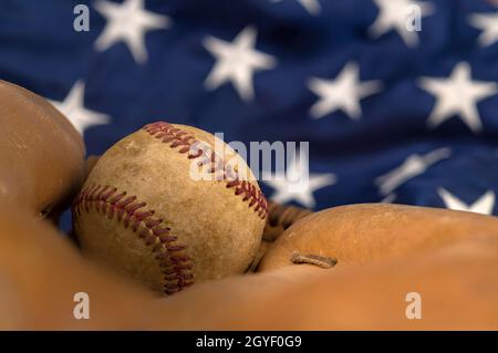 Il primo piano di un vecchio baseball e di un guanto contro la bandiera americana mette in evidenza uno degli sport più popolari del paese. Foto Stock