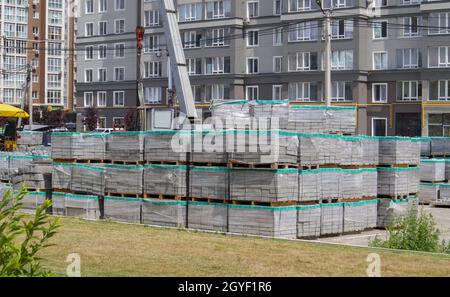 Sul cantiere sono presenti molte nuove lastre grigie per pavimentazione su pallet rivestiti in plastica. Pavimentazione di sentieri pedonali su una strada cittadina. Primo piano. REP Foto Stock