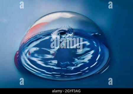 Superficie blu con bolla pulita contenente increspature da due gocce d'acqua che si scontrano nell'aria Foto Stock