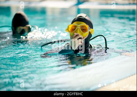 Subacqueo femminile e subacqueo maschile in attrezzatura subacquea, lezione di immersione in scuola subacquea. Insegnare alle persone a nuotare sott'acqua, piscina interna su bac Foto Stock