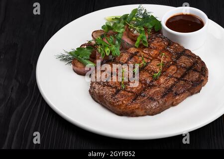 Bistecca di angus nero grigliata su piatto bianco su fondo di legno nero Foto Stock