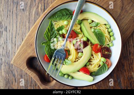 Insalata di pasta con piselli verdi, avocado, pomodori ciliegini e basilico su rustico fondo di legno. Vista dall'alto. Foto Stock