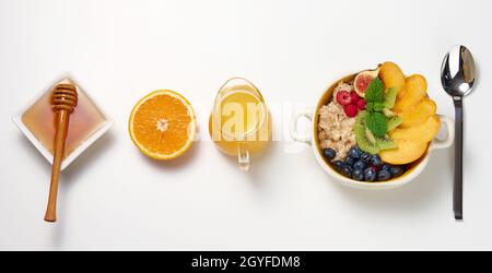 piatto con farina d'avena e frutta, mezzo succo d'arancia maturo e spremuto di fresco in un decanter trasparente in vetro, miele in una ciotola su un tavolo bianco. Sano Foto Stock