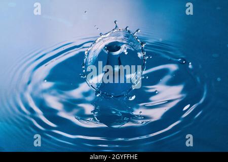 Due gocce d'acqua si scontrano su una superficie blu pulita Foto Stock