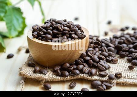 Caffè in grani medio arrostito in ciotola di legno con foglie al mattino fresco. Foto Stock