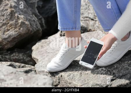 Donna che raccoglie il telefono cellulare danneggiato dalla pietra all'aperto, primo piano Foto Stock