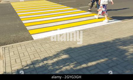 due pedoni che attraversano la strada su una nuova marcatura giallo-bianca di un passaggio pedonale, sicurezza della vita, concetto di trasporto. Foto Stock