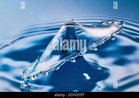 Due gocce d'acqua si scontrano con increspature sull'acqua blu Foto Stock