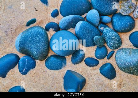 Pietre blu e nere contro una spiaggia sabbiosa Foto Stock