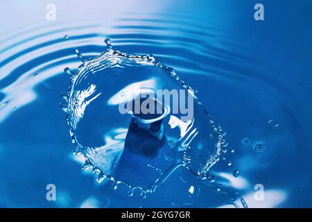 Due gocce d'acqua si infrangono e creano onde sull'acqua blu Foto Stock