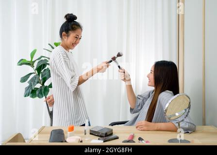 Due ragazze adolescenti asiatiche giocano a scherma con le spazzole per il trucco. I compagni di stanza hanno divertimento imparare a fare il make-up per gli amici asiatici. Goditi un weekend di svago a casa tua. Foto Stock