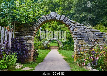Arcate in pietra nei pressi di una foresta che conduce in un giardino con fiori e gradini in pietra Foto Stock