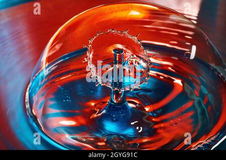 Due gocce d'acqua che si incontrano nell'aria all'interno della bolla su acqua blu e rossa Foto Stock
