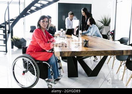 Donna latina transgender in sedia a rotelle che partecipa a un incontro d'affari con il team nella sala conferenze di Città del Messico Foto Stock